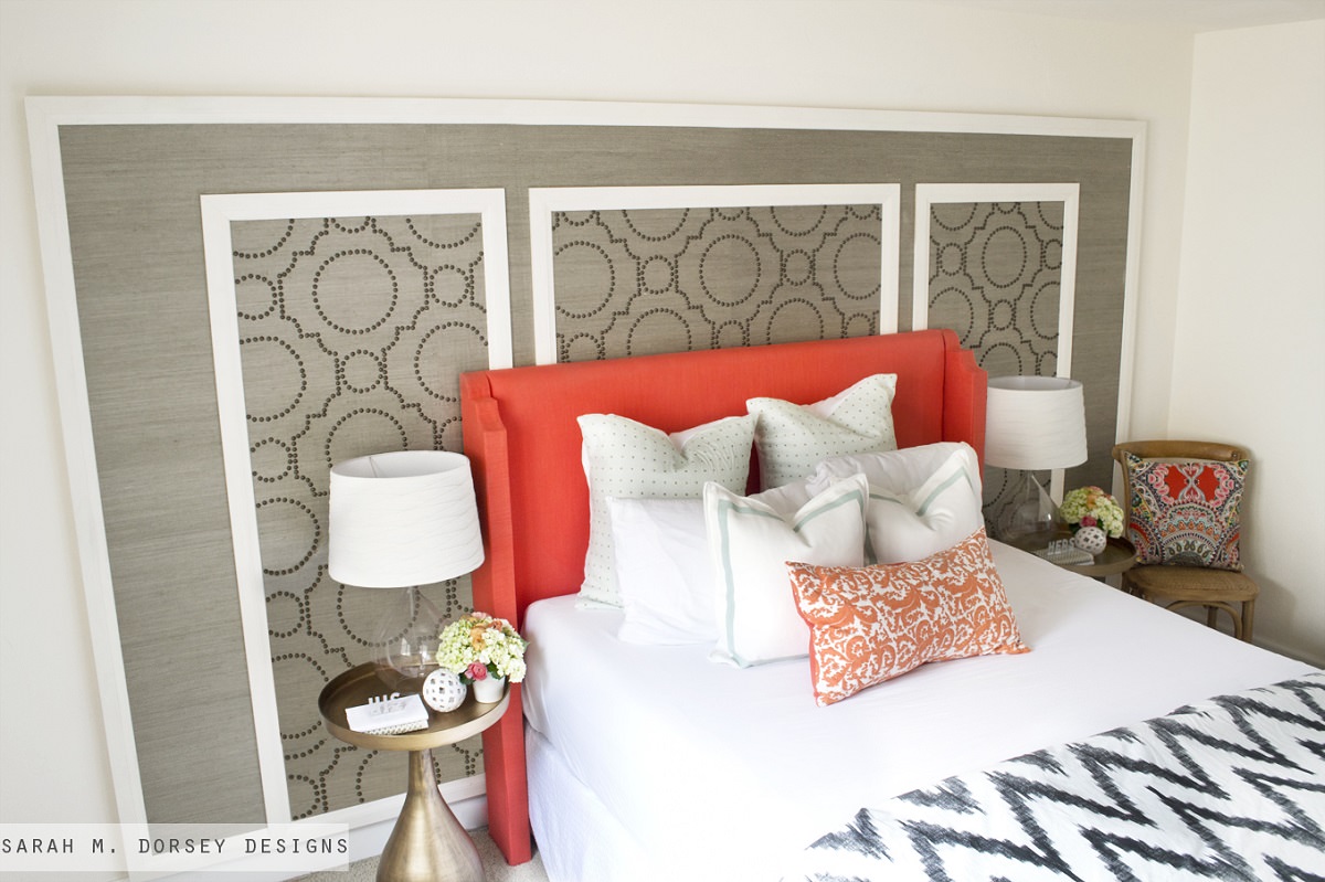 اتاق خوابی که دارای دیوار سفید رنگ و تاج تخت نارنجی می باشد و سطح داخلی دیوار پشت تخت که قاب بندی شده است، کاغذ دیواری شده است